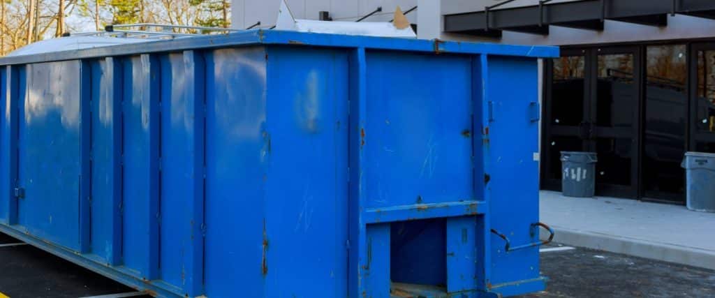 Large blue dumpster positioned outside a building under renovation during the day in an urban setting