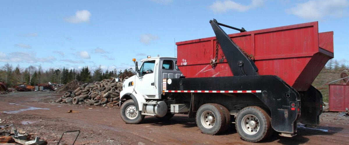 Heavy dump truck unloading materials in a construction site near a scrapyard during a sunny day