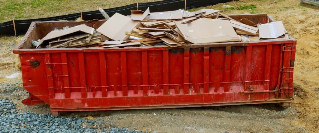 Construction site showing a red dumpster filled with cardboard waste at a building location during the daytime