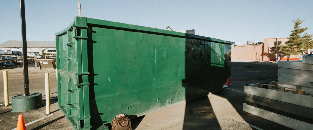 Green dumpster sits in a construction area during daylight under clear skies in an urban environment