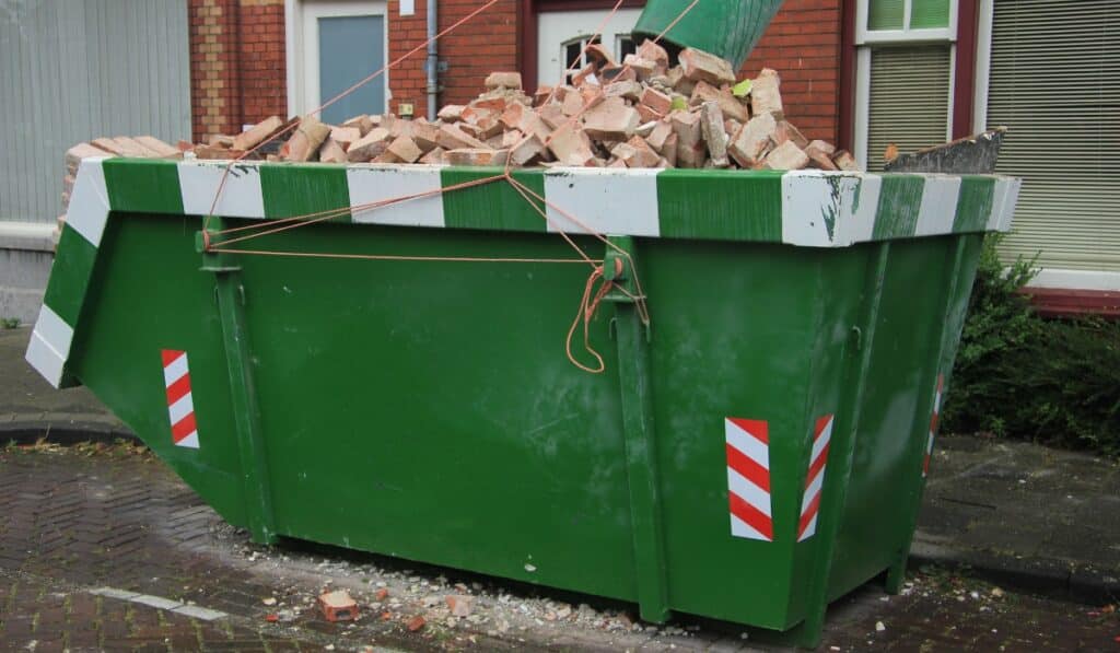 Green dumpster filled with bricks.