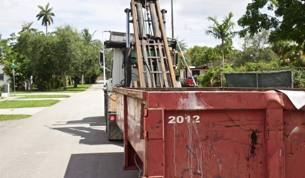 Truck delivering dumpster on street.