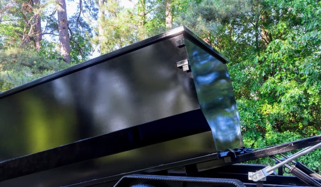 Black dumpster against green trees
